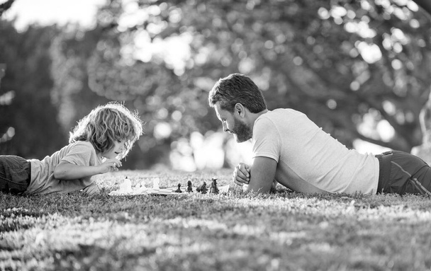 šťastná rodina tatínek a syn dítě hrát šachy na zelené trávě v parku venkovní, erudované. - Fotografie, Obrázek