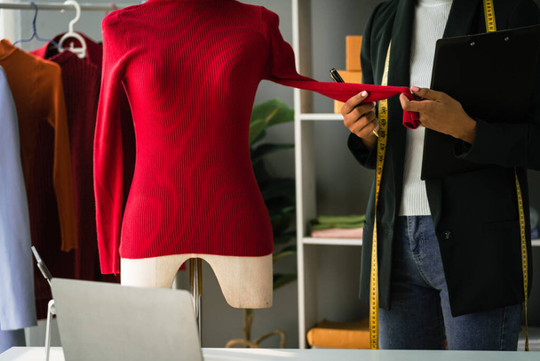 Afrikaans-Amerikaanse ontwerper vrouw met klembord en het controleren van details van trui op etalagepop. - Foto, afbeelding
