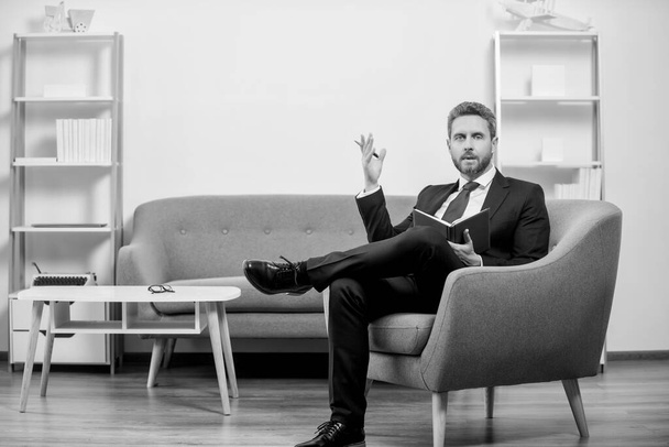 mature businessman gesturing in suit sit in office reading book. - Photo, Image