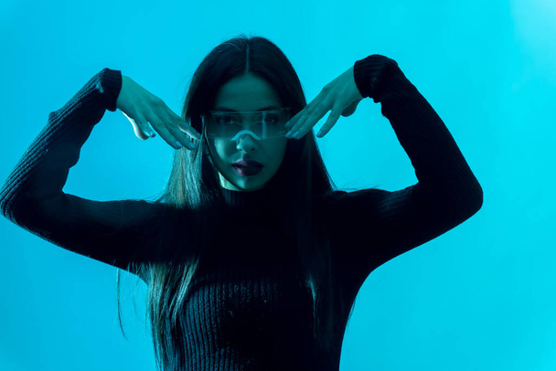 Metaverse technology concept. Portrait of woman in futuristic glasses with led light on a blue background - Fotó, kép