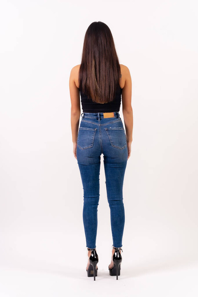 Brunette woman in casting photos on a white background, in jeans and a black t-shirt with her back turned - Foto, afbeelding