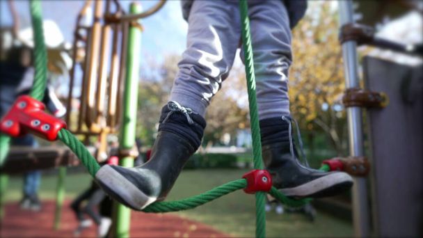 Closeup Child feet wearing boots holding into rope at playground. Active little boy kid legs - Фото, изображение