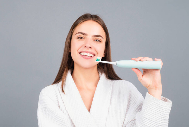 Electric toothbrush. Beauty portrait of a happy beautiful woman brushing her teeth with a toothbrush isolated background - Фото, зображення