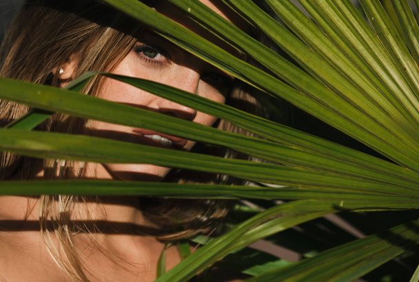Portrait of tender woman looking out of tropical palm leaf. Beauty face closeup - Foto, Imagen