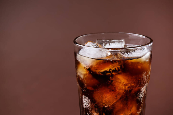 Een glas cola drinken met ijsblokjes. Verse koude zoete cola drank met ijs op bruine achtergrond met kopieerruimte. - Foto, afbeelding