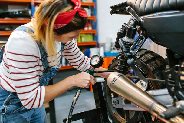 オートバイのタイヤ空気圧を工場でチェックする機械的な女性 - 写真・画像