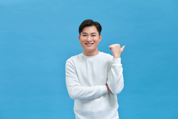 Young handsome man pointing to the back behind with hand and thumbs up, smiling confident - Photo, image