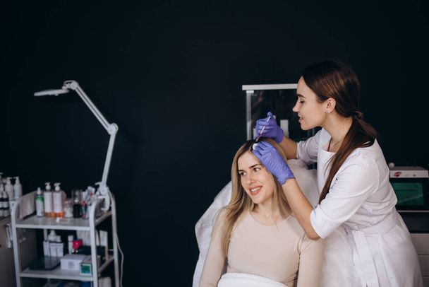 Young beautiful woman receiving hair mesotherapy injections from a professional trichologist. Doctor's hands in pink gloves. Hair treatment in cosmetology using mesotherapy. Injection to the head - Photo, Image