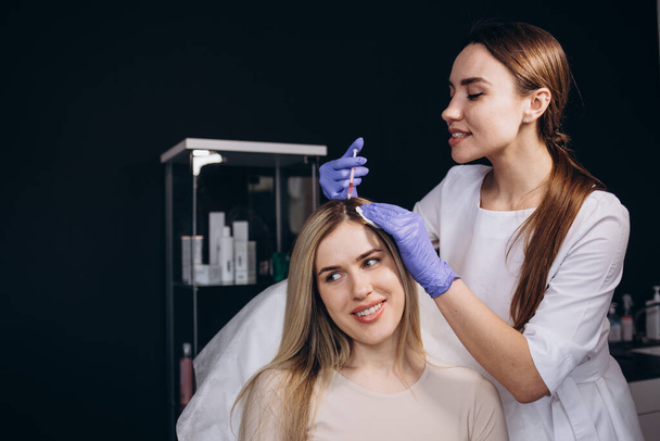 Young beautiful woman receiving hair mesotherapy injections from a professional trichologist. Doctor's hands in pink gloves. Hair treatment in cosmetology using mesotherapy. Injection to the head - Photo, Image