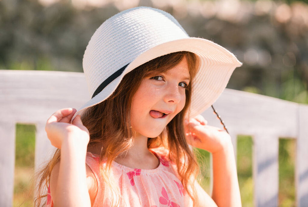 Funny kids face with tongue. Portrait of funny child girl in summer park. Face close up of cute teen girl outdoor. Cute little girl swinging on the meadow in summer day - 写真・画像