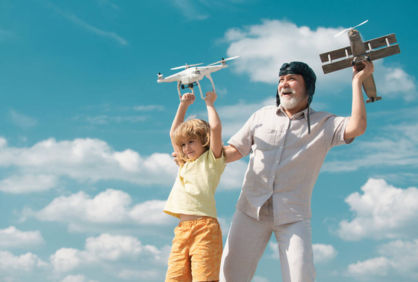 Old grandfather and young child grandson hold plane and drone quad copter against sky. Child pilot aviator with plane dreams of flying - Foto, Imagen