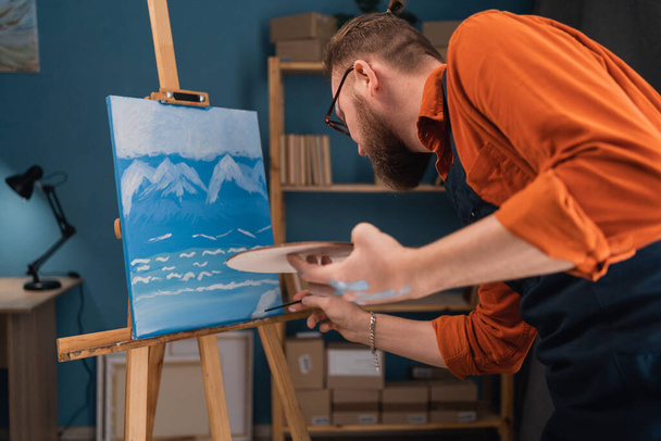 Working artist concentrating on his painting while creative a masterpiece. Male artist working on a painting in bright studio daylight. Copy space - Foto, Bild