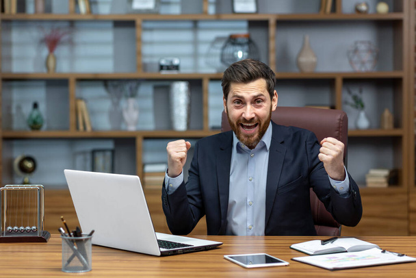 Portrait of mature senior businessman in office, man looking at camera and holding hands up super power and superhero gesture, successful investor using laptop inside building. - Foto, Imagem