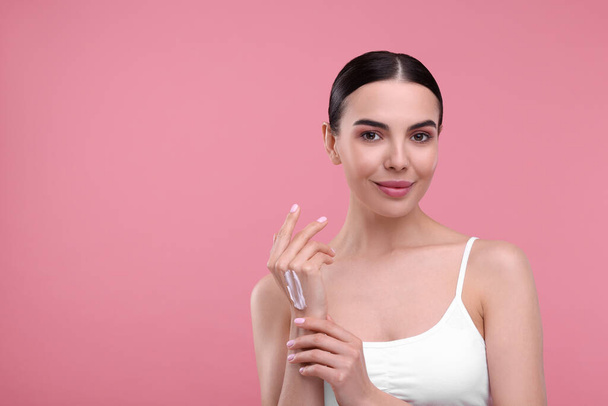 Beautiful woman with smear of body cream on her hand against pink background, space for text - Foto, afbeelding