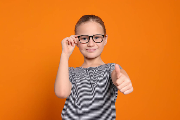 Cute girl in glasses showing thumb up on orange background - Fotoğraf, Görsel