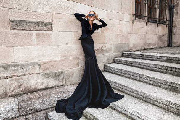 Elegant luxury evening fashion. Glamour, stylish elegant woman in black long evening gown dress is posing in the city outdoor. Female model in amazing long dress. Outdoor shoot. Vogue. Couture. - Fotó, kép