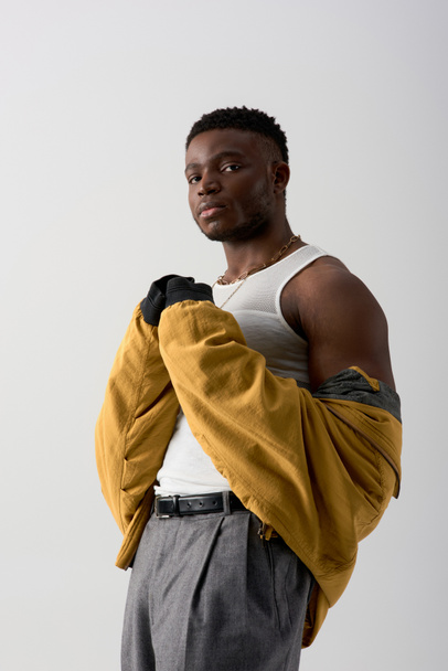 Portré fiatal és magabiztos afro-amerikai férfi bomber kabát és ujjatlan póló áll elszigetelve szürke, kortárs fotózás jellemző stílusos öltözékben, izmos - Fotó, kép
