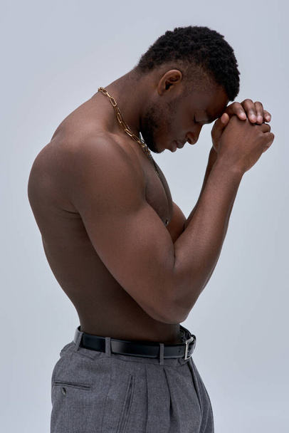 Side view of muscular and shirtless african american man in pants and golden necklaces standing isolated on grey, confident and modern pose, fashion shoot - Foto, immagini