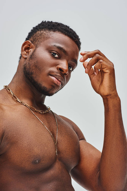Portrait of muscular afroamerican man with golden necklaces looking at camera while standing isolated on grey, confident and modern pose, fashion shoot - Valokuva, kuva