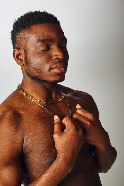Portrait of muscular and shirtless african american man with closed eyes touching necklaces isolated on grey, confident and modern pose, fashion shoot - Fotografie, Obrázek