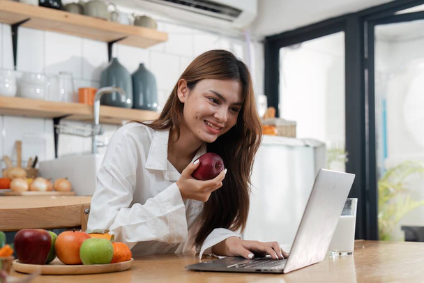 Asiática joven uso de la computadora portátil en la cocina en casa. - Foto, Imagen