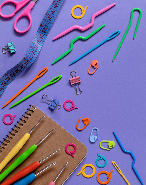Notebook and colorful knitting tools on a purple background. Top view. Copy space. - Foto, imagen