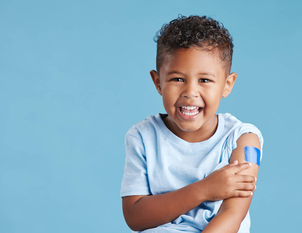 Portrait, happy and kid with plaster in studio isolated on a blue background mockup space. Face, smile and boy child with bandage after vaccine, injury or wound for healthcare, first aid and excited - Photo, Image