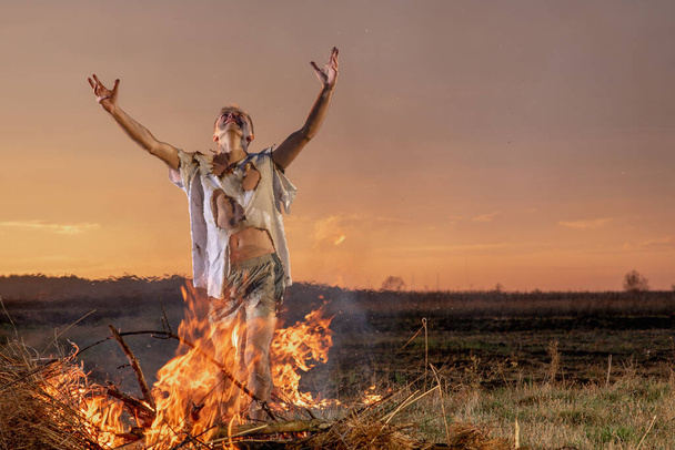 молодой парень плачет в огне в сгоревшей одежде прося Бога о помощи, войне, разрушении дома, человеческом разочаровании - Фото, изображение