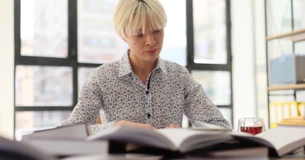 Zaměřená studentka čte knihy, aby našla informace pro absolventský projekt u stolu v knihovně. Soustředěná žena s krátkými blond vlasy zkoumá materiál zpomalení - Záběry, video