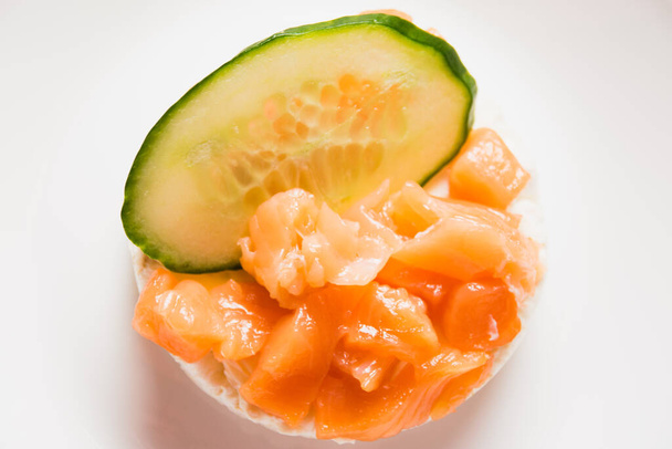 Sandwich with red fish and cucumber close-up on a white plate. Salted salmon on crispy rice bread on a wooden background. - 写真・画像