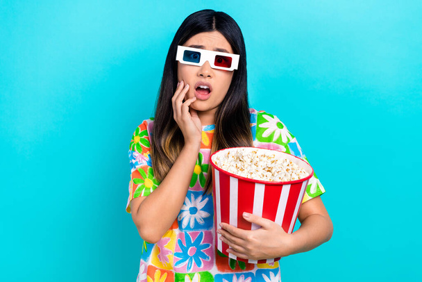 Fénykép a ijedt megdöbbent hölgy visel virágmintás póló eszik popcorn néz horror film elszigetelt kék háttér. - Fotó, kép