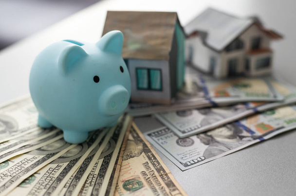 piggy bank for money and a house model with dollars on a white background. buying a property. the concept of buying and selling houses and apartments - Foto, Imagen