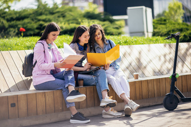 Группа девочек-коллажисток сидит на скамейке и учится в школе - Фото, изображение