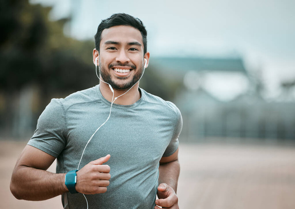 Fitness, portrait and man running with earphones for music, radio or sport podcast for motivation. Sports, exercise and male athlete runner doing outdoor cardio workout for race or marathon training - Photo, Image