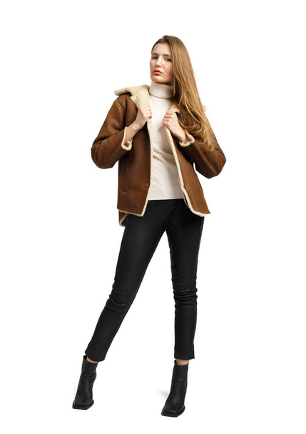 Ein junges stilvolles Mädchen in einem kurzen braunen Schaffell-Mantel, eine warme Jacke posiert wunderschön auf weißem Hintergrund. Modische, stylische, bequeme Oberbekleidung, Bekleidungswerbung. - Foto, Bild