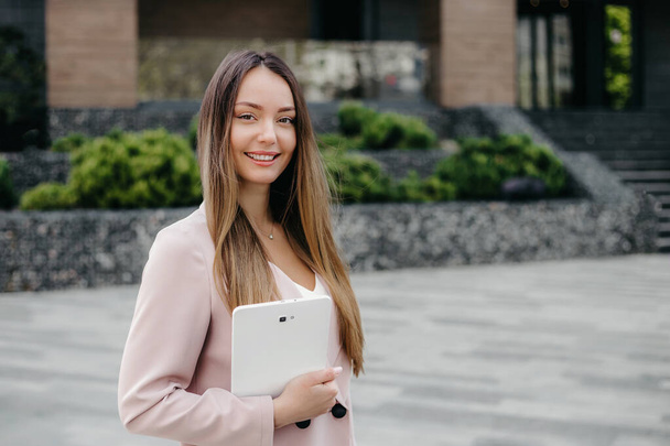 Happy caucasian business woman in a beige business suit smiling holding a tablet in her hands and looking at camera. Internet marketer, financial analyst, HR manager - Фото, зображення