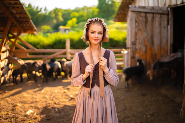 Gyönyörű fiatal vidéki lány középkori ruhában és kalapban pózol egy farmon. Csinos szőke modell vidéki művészet fotó.  - Fotó, kép