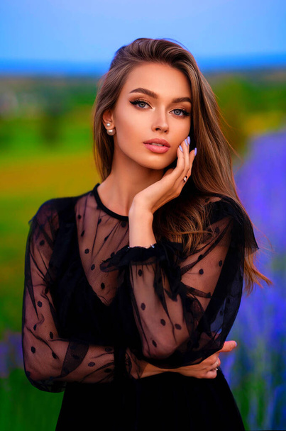 Porträt eines schönen Mädchens in einem schwarzen transparenten Kleid, das in einem bunten Lavendelfeld steht. Kunstwerk einer romantischen Frau . - Foto, Bild