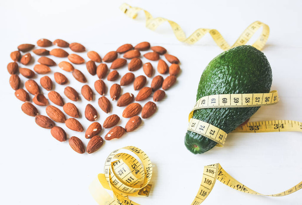 Almond heart and avocado with tape measure.  Weight loss diet. Loving healthy lifestyle. Vegan concept. Proper nutrition. Sport food. Nuts and vitamins. - Photo, Image