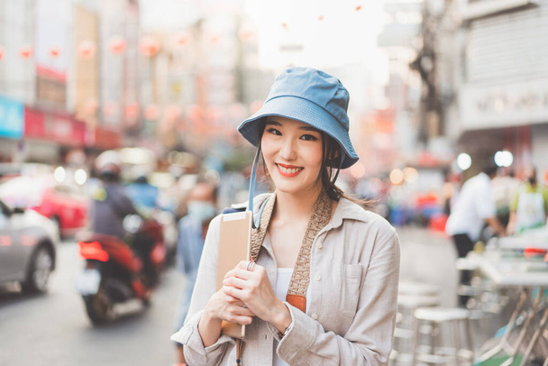 Attractive happy young adult asian woman traveller wear blue hat and backpack. Solo traveling with modern technology portable device lifestyle at city outdoor on day. Staycation summer trip concept. - Φωτογραφία, εικόνα