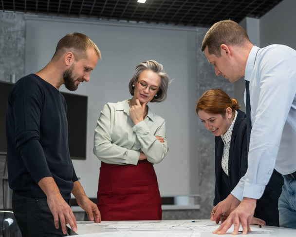 Four business people review and discuss blueprints. Designers engineers at a meeting - Foto, Bild