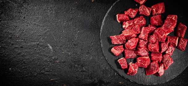 Pieces of raw beef on a stone board. On a black background. High quality photo - Photo, Image