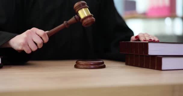 Judge in black mantle hits gavel on sound block sitting at wooden table. Woman puts hand on legislation books as justice symbol in court office slow motion - Footage, Video