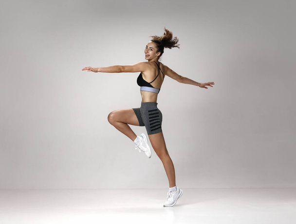 Dynamic image of happy, smiling, fit young girl in sportswear training against gray studio background. Wellness. Concept of sportive lifestyle, beauty, body care, fitness, health - Fotó, kép