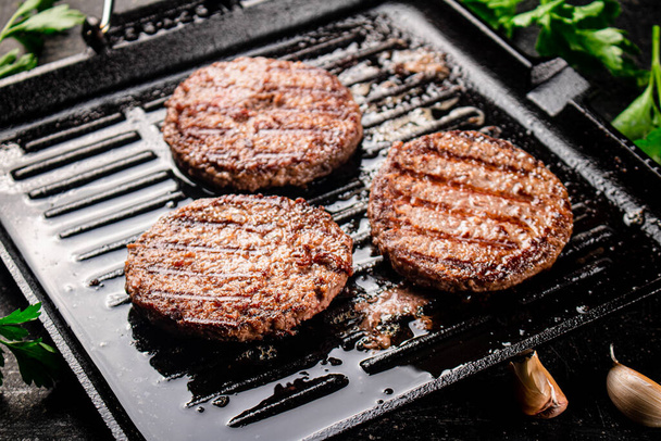 Cooking a delicious grilled burger on a pan with oil bubbles. On a black background. High quality photo - 写真・画像
