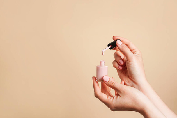 Esmalte de uñas rosa claro en manos femeninas sobre fondo beige, espacio para copiar - Foto, imagen
