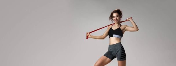 Portrait of young girl in sportswear with slim, fit boy posing with fitness expanders against gray studio background. Concept of sportive lifestyle, beauty, body care, fitness, health. Banner - Photo, Image