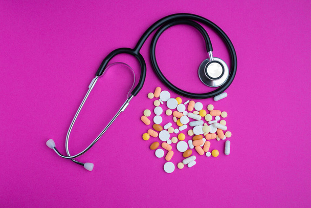 Concept medisch onderzoek, diagnose en behandeling, stethoscoop op roze achtergrond met mix pillen als vraagteken geïsoleerd - Foto, afbeelding