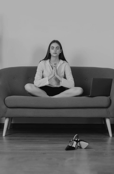 Meditation woman in a modern workplace doing yoga exercise on sofa at workplace in a modern office. Employee feel balance harmony relaxation. Calm accountant girl on sofa in office - Фото, зображення