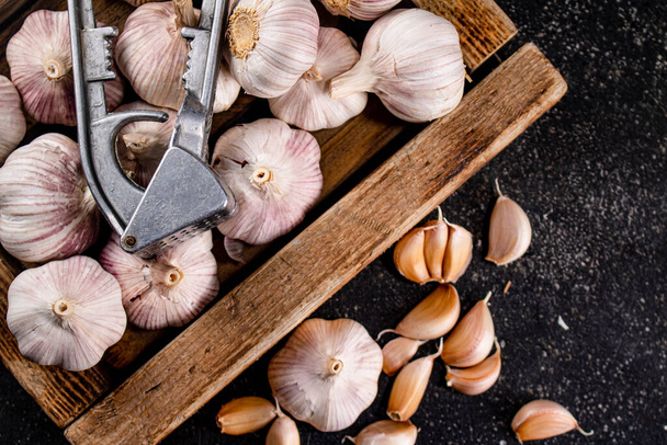 Garlic on a wooden tray with a garlic press. On a black background. High quality photo - Foto, Bild